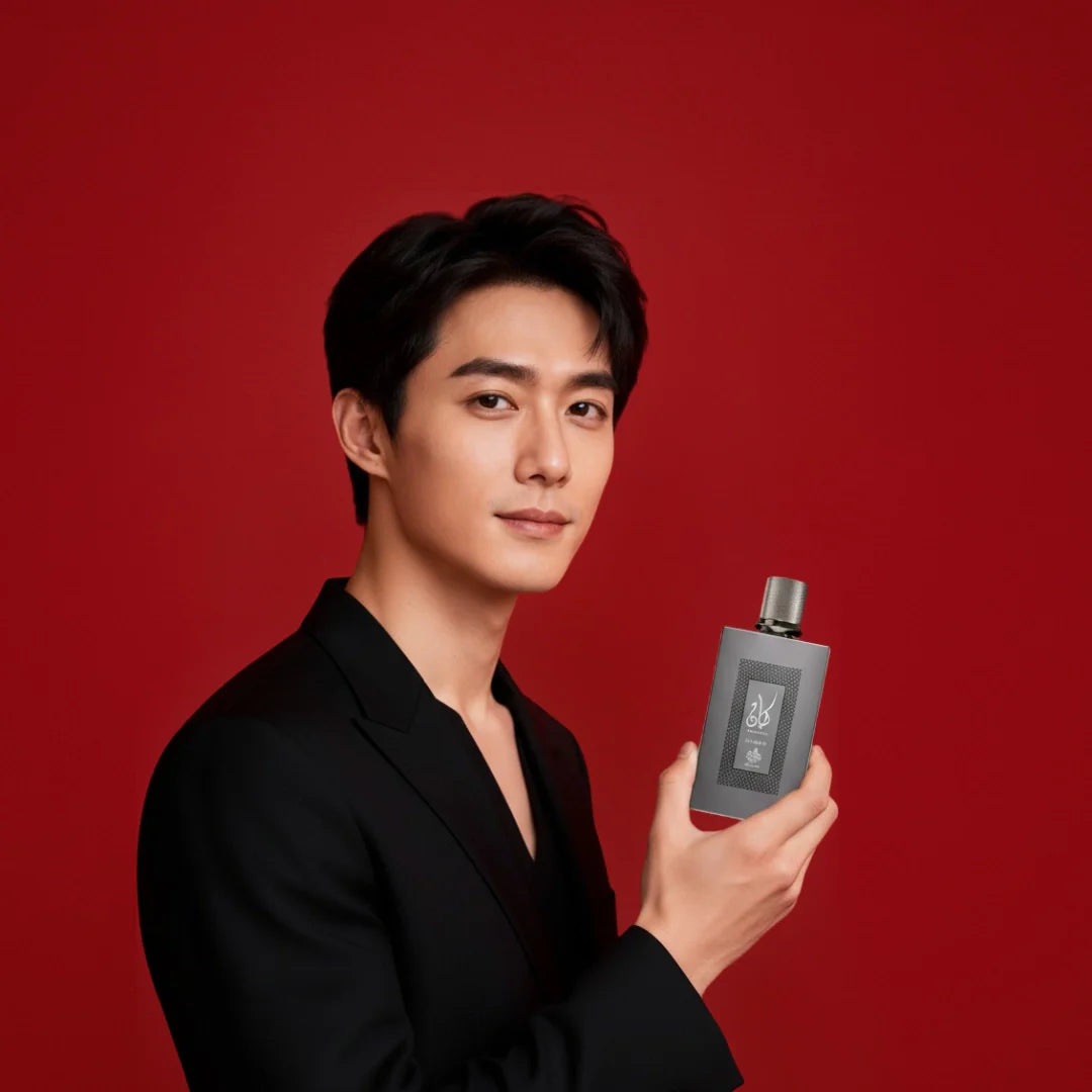 Oudelier | Men’s perfume collection — a man in a black suit holding a sleek gray perfume bottle against a red background.