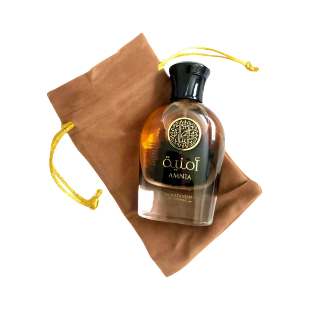 Al Wataniah Amnia オードパルファム 100ml/3.4fl.oz. - 黄色と白色のグラデーションボトル、黒色のキャップ、円形メダリオン、ベージュの巾着袋付き、白い背景
